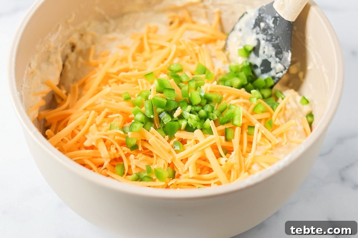Adding cheese and diced jalapenos to a gray bowl.
