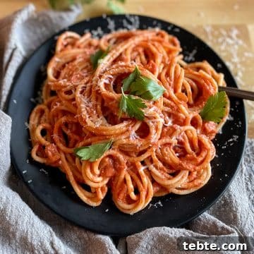 Twirled spaghetti on a black plate topped with parsley and parmesan cheese.