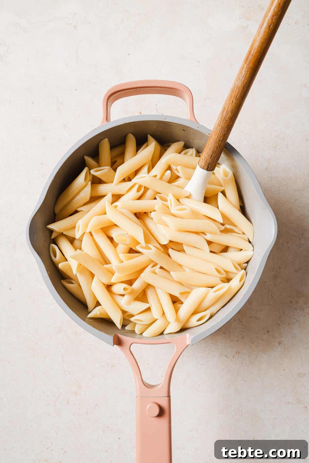 Creamy Tuna Pesto Pasta Recipe for Quick Weeknight Meals 4 Penne pasta in a pan with a wooden spoon.