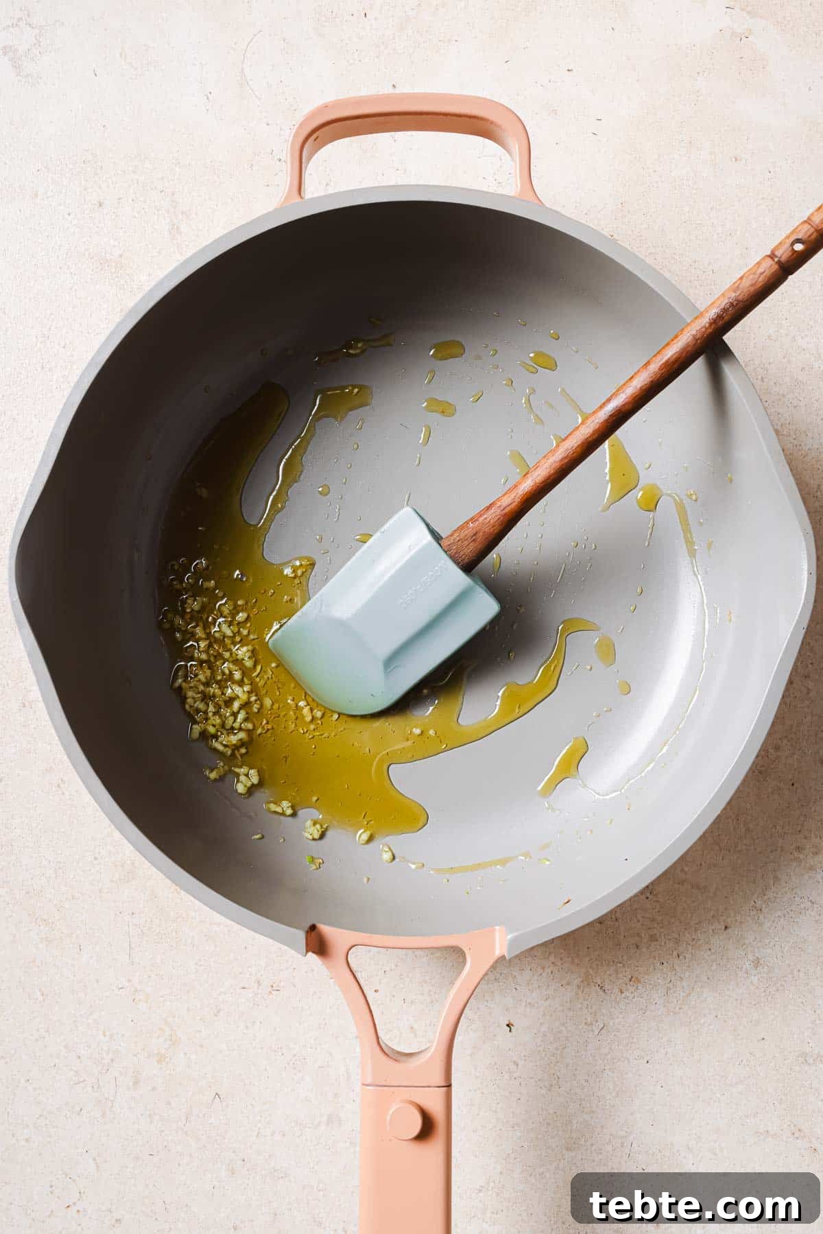Creamy Tuna Pesto Pasta Recipe for Quick Weeknight Meals 5 A frying pan with olive oil, garlic, and a wooden spatula.