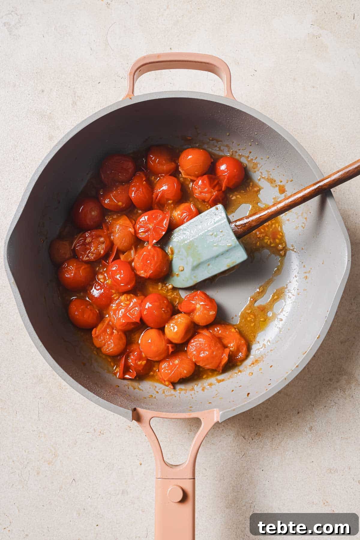 Creamy Tuna Pesto Pasta Recipe for Quick Weeknight Meals 6 A frying pan with tomatoes and a wooden spatula.