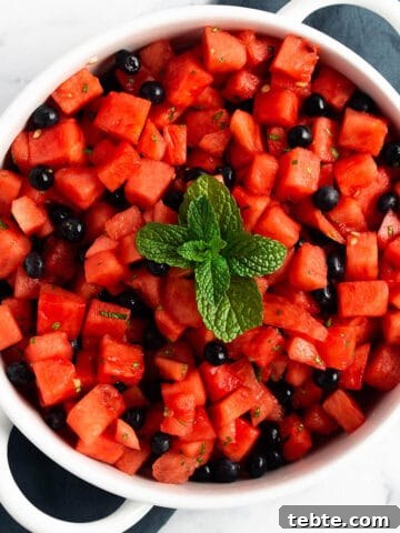 A white serving tray with cubed watermelon, blueberries and fresh mint on top.