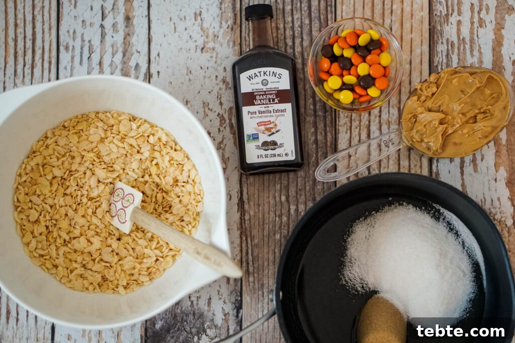 No-Bake Rice Krispies Cookies Recipe — Quick Treats in Minutes 4 A bowl of Rice Krispies, a bottle of vanilla extract, a serving of Reese's pieces, 3/4 cup of peanut butter, and a small saucepan of corn syrup, brown sugar, and granulated sugar.