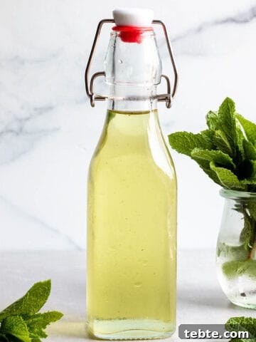 A glass flip lock bottle with a green simple syrup and fresh mint leaves.