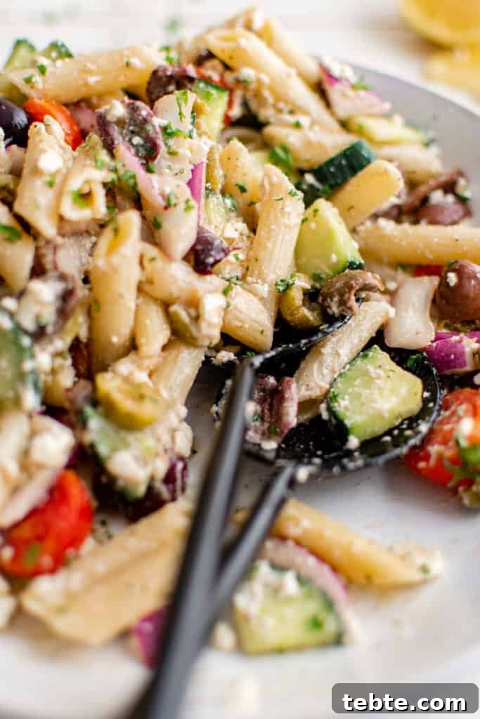 Mediterranean Greek Pasta Salad with Feta and Olives 4 Close up view of tongs holding pasta salad.