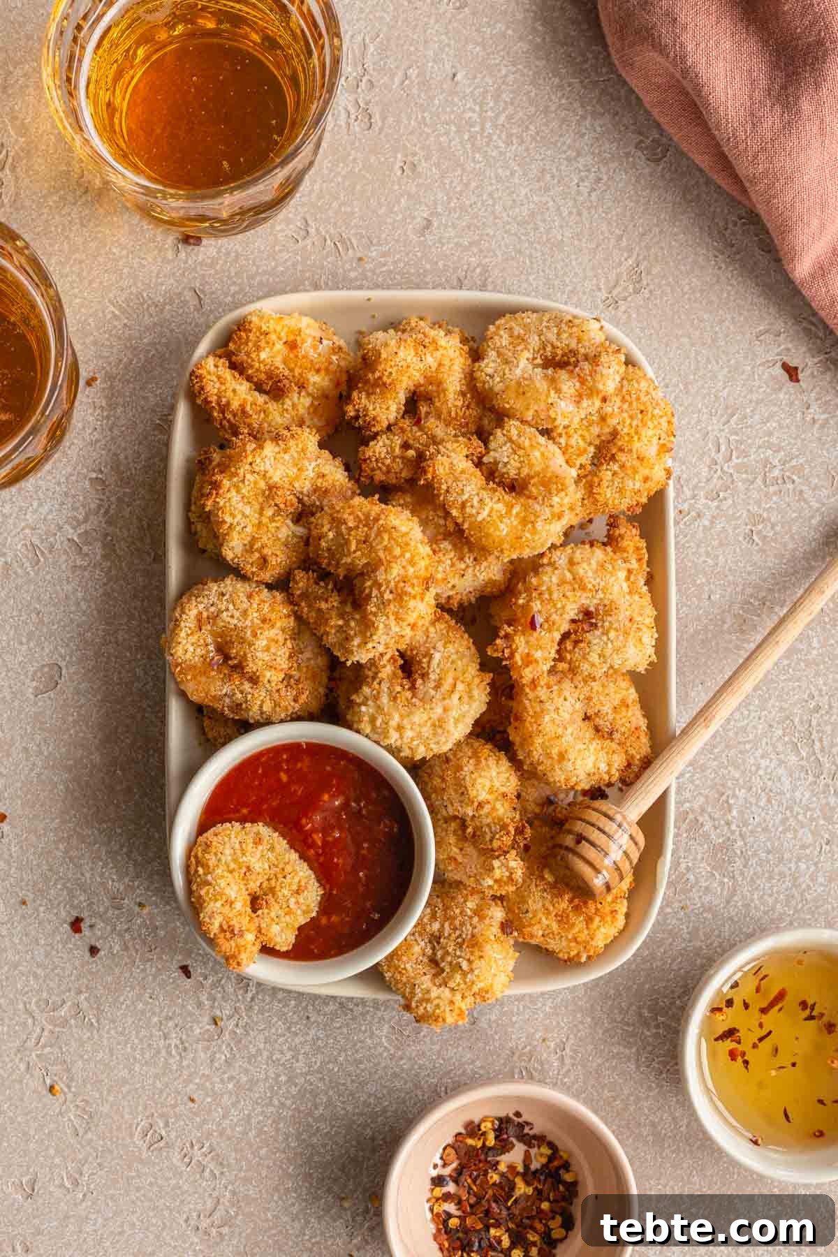 Crispy Air Fryer Breaded Shrimp Recipe for Quick Dinner 2 Air fryer breaded shrimp piled on a rectangular plate with bowls of seafood sauce and honey in view.