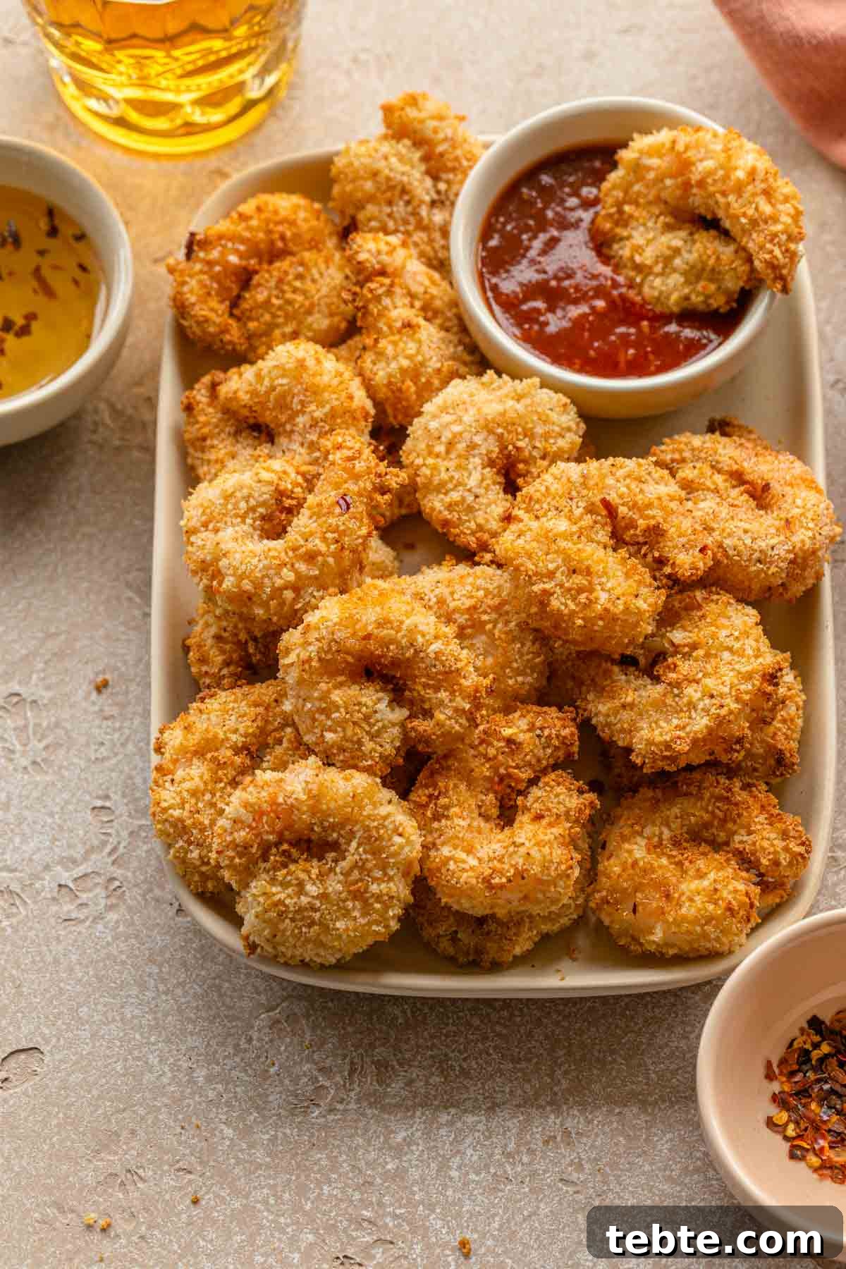 Crispy Air Fryer Breaded Shrimp Recipe for Quick Dinner 7 Close up of crispy breaded shrimp on a plate with seafood sauce in the background.