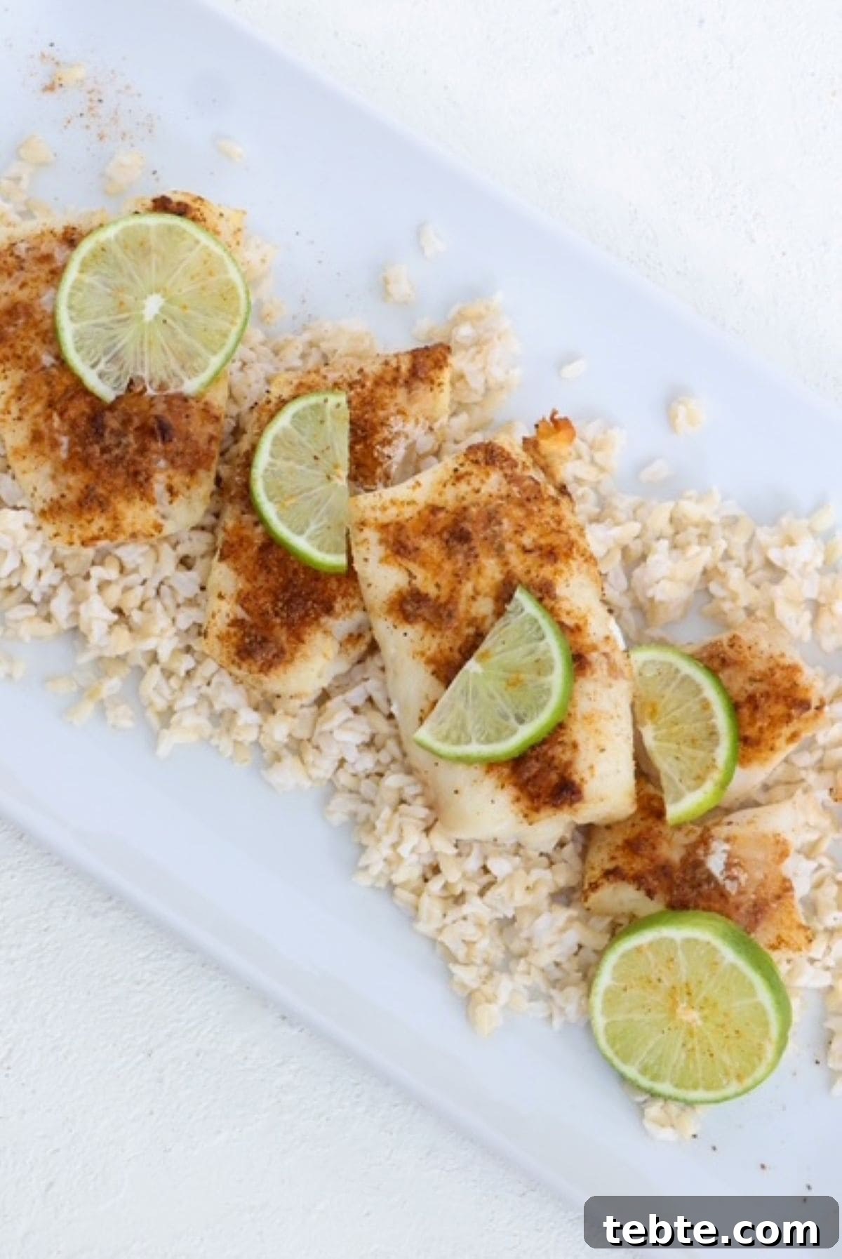 Air Fryer Cod with 3 Ingredients — Quick Crispy Recipe 2 Cooked cod fillets topped with seasoning and fresh lime slices on a white serving dish.