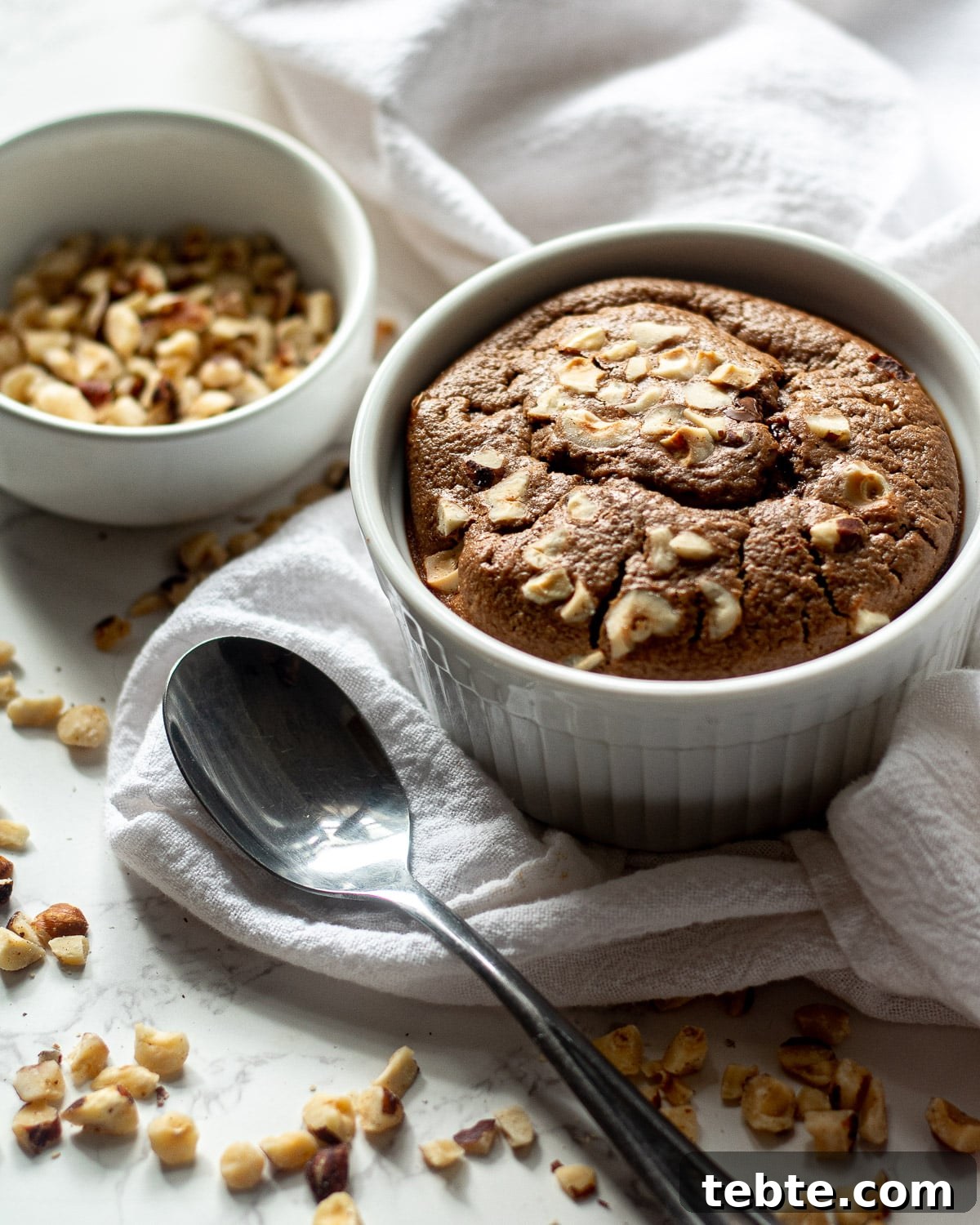 Nutella Baked Oats Recipe: Creamy Chocolate Hazelnut Breakfast 4 nutella baked oats in the ramekin with hazelnuts in a bowl and scattered around