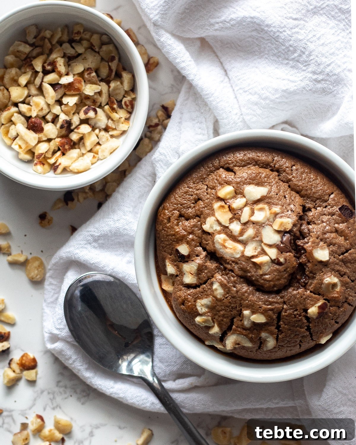 Nutella Baked Oats Recipe: Creamy Chocolate Hazelnut Breakfast 5 nutella baked oats in the ramekin with hazelnuts in a bowl and scattered around
