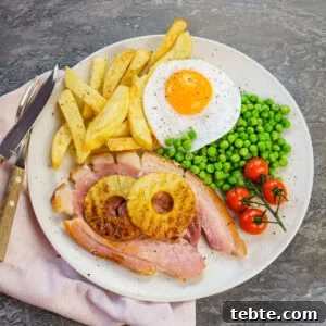 Classic Gammon Steak with Fried Egg and Chips 3 Gammon egg and homemade chips served with vined cherry tomatoes, peas and two pineapple rings on a white plate