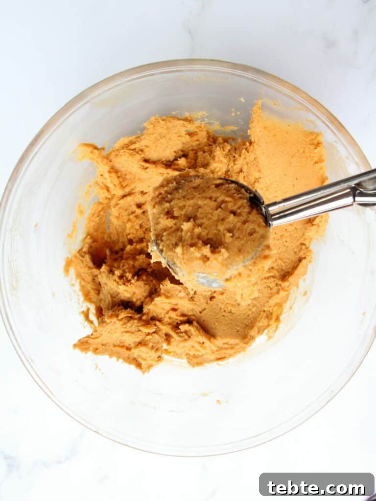 Pumpkin Cheesecake Cookies Recipe — Soft, Creamy Fall Treat 12 pumpkin cookie dough in transparent bowl scooped with ice cream scooper
