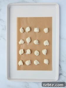 Pumpkin Cheesecake Cookies Recipe — Soft, Creamy Fall Treat 20 cheesecake filling dolloped onto brown parchment paper