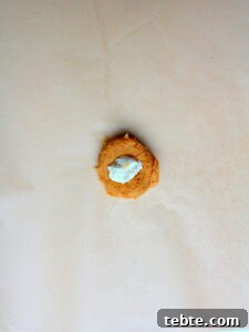 Pumpkin Cheesecake Cookies Recipe — Soft, Creamy Fall Treat 26 pumpkin cookie on brown parchment paper filled with cheesecake filling