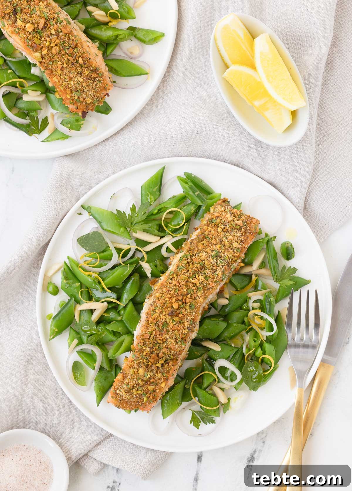 Oven-Roasted Salmon with Pistachio Crust 2 Pistachio crusted salmon filets with a snap pea salad on white plates.