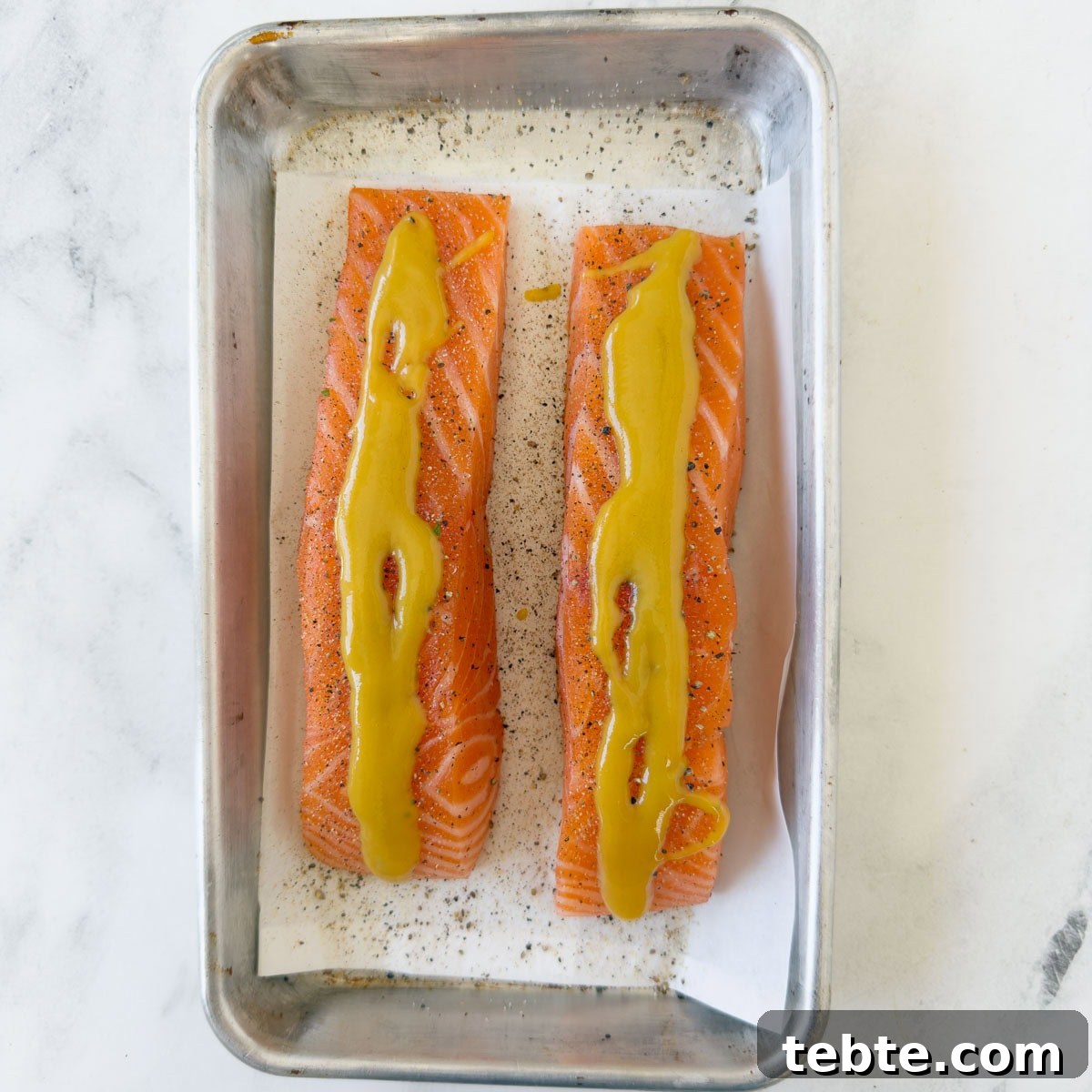 Oven-Roasted Salmon with Pistachio Crust 5 Salmon fillets topped with honey mustard sauce on a sheet pan with parchment.