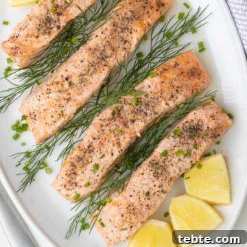 Close up of a platter of salmon filets with lemon and herbs on a table.