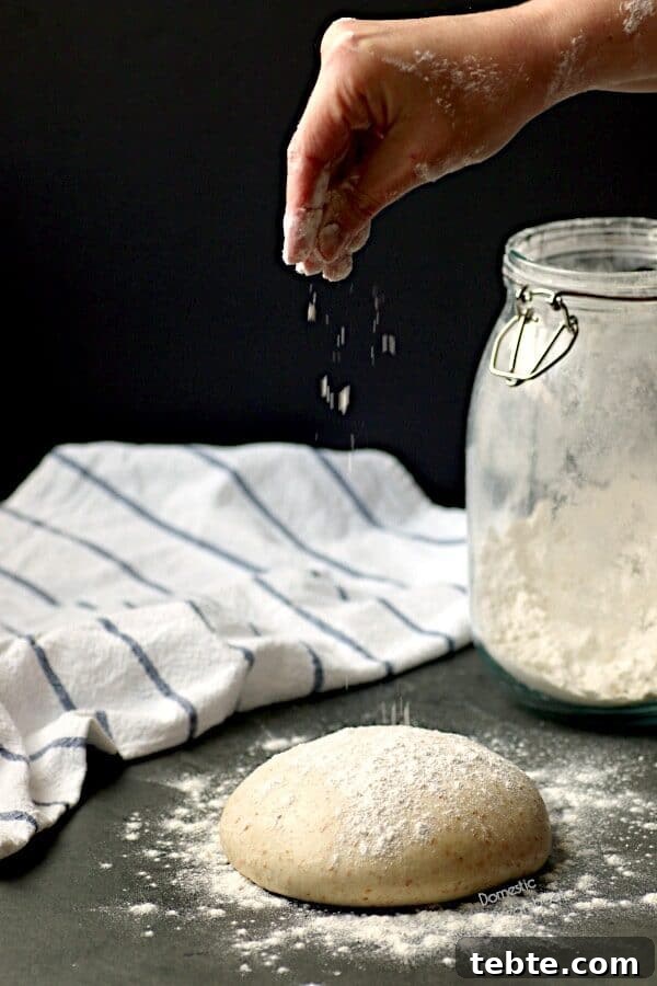 A hand sprinkling flour on a ball of homemade pizza dough.