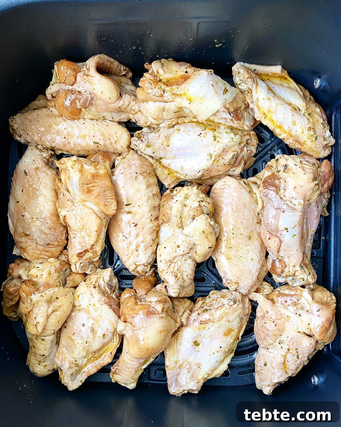overhead shot of raw, uncooked marinated chicken wings in the air fryer basket