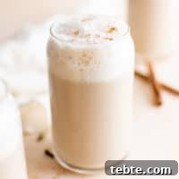 Glass of chai latte with frothed milk and cinnamon sticks.