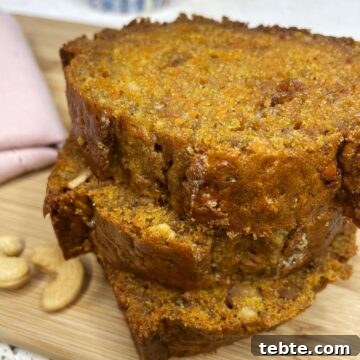 Three slices of carrot loaf on a wooden board with a pink towel in the background.