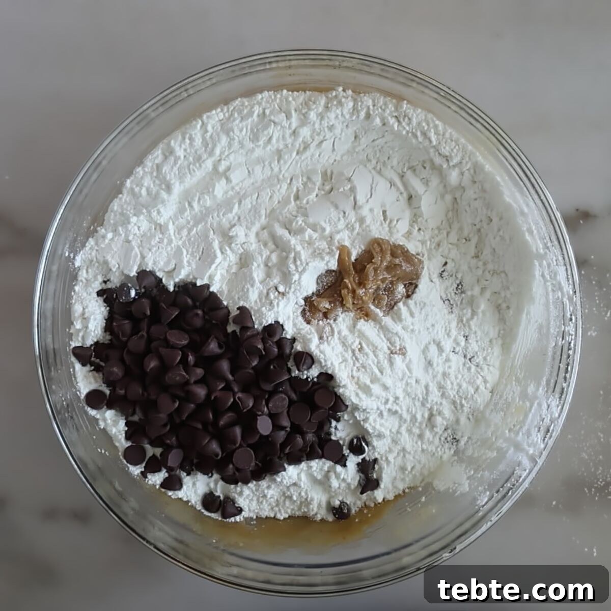 Gluten-Free Flag Cookie Cake Recipe for Patriotic Celebrations 9 flour and chocolate chips on top of wet ingredients in glass bowl.