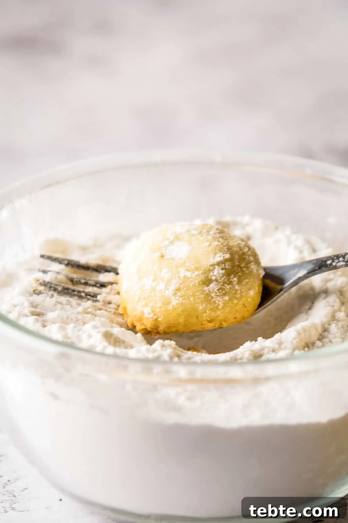 Close up of fork being used to dip cookies into powdered sugar.