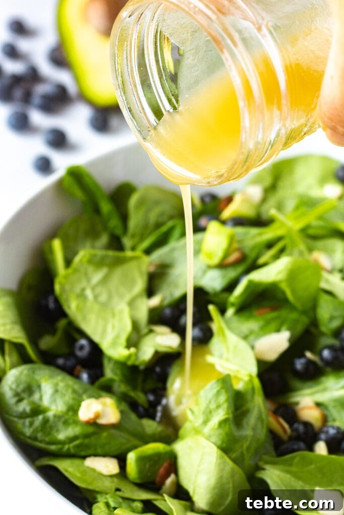 10-Minute Blueberry & Spinach Salad with Sweet Honey Vinaigrette 8 Close up of pouring white balsamic vinaigrette onto a blueberry spinach salad that's in a white serving bowl.