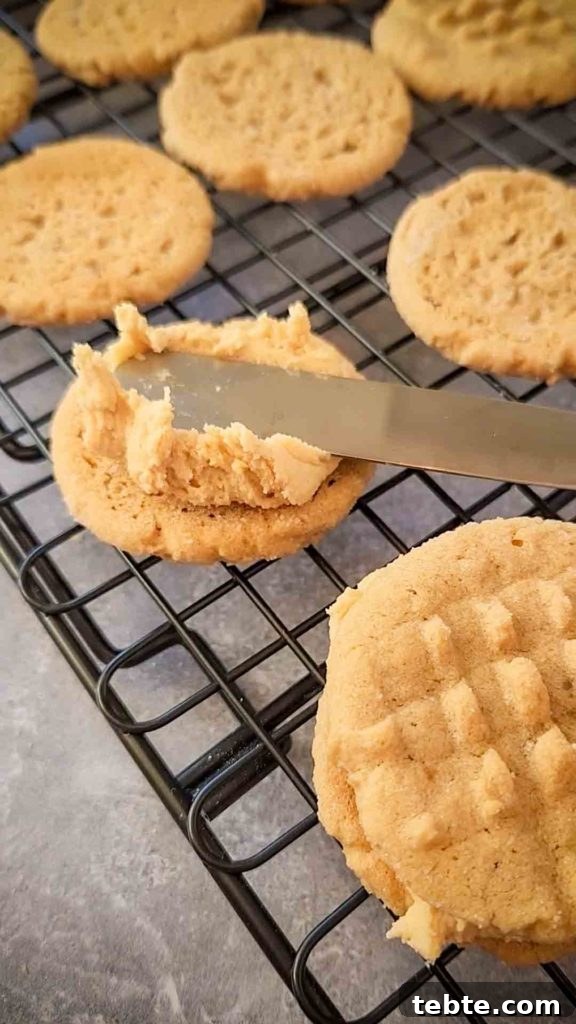 Gluten-Free Nutter Butter Cookies Recipe: Homemade Peanut Butter Sandwich Cookies 3 a knife is spreading peanut butter frosting on the smooth side of a peanut butter cookie.