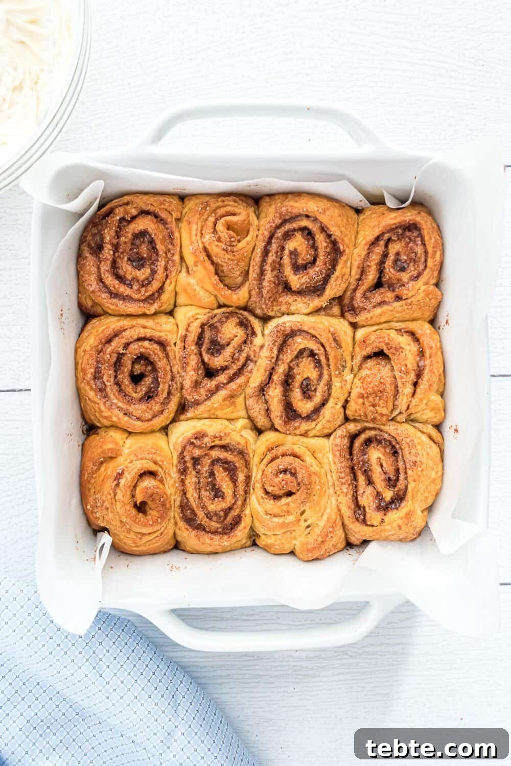 Quick Crescent Roll Cinnamon Swirl Rolls 5 A white baking dish lined with parchment paper holds twelve baked cinnamon rolls arranged in a 3x4 grid.