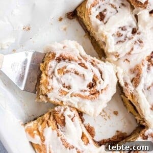 Quick Crescent Roll Cinnamon Swirl Rolls 11 A close-up of a frosted cinnamon roll being lifted from a baking dish with a metal spatula.