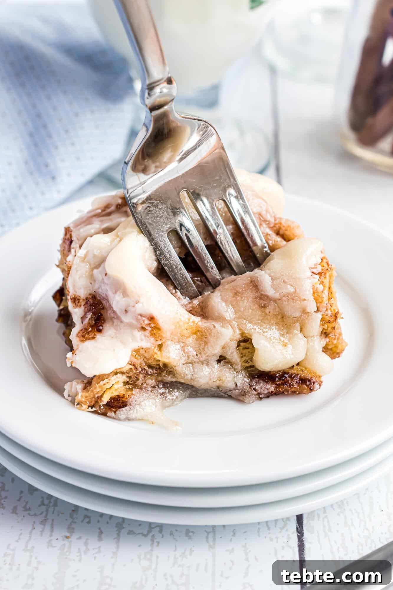 Quick Crescent Roll Cinnamon Swirl Rolls 3 A fork cutting into a frosted cinnamon roll on a stack of white plates.