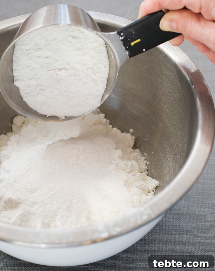 How to Make Natural DIY Body Powder at Home 4 A half-filled measuring cup adding into a stainless mixing bowl with cornstarch