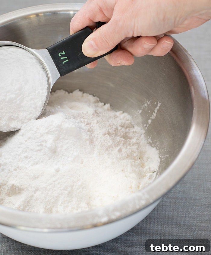 How to Make Natural DIY Body Powder at Home 5 A measuring cup filled with baking soda ready to mix in with cornstarch on a stainless mixing bowl