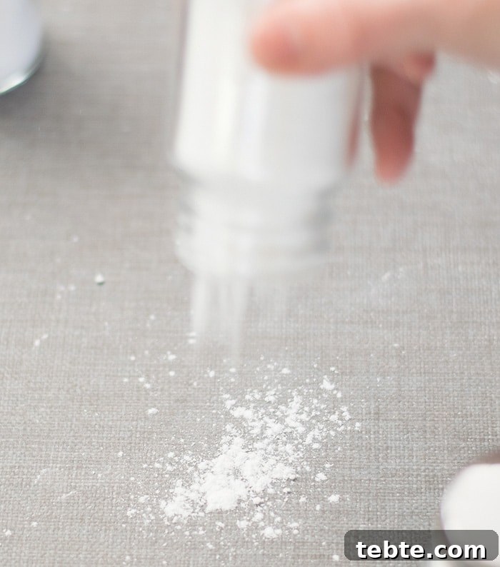 How to Make Natural DIY Body Powder at Home 8 A hand pouring the DIY Body Powder on a grayish linen