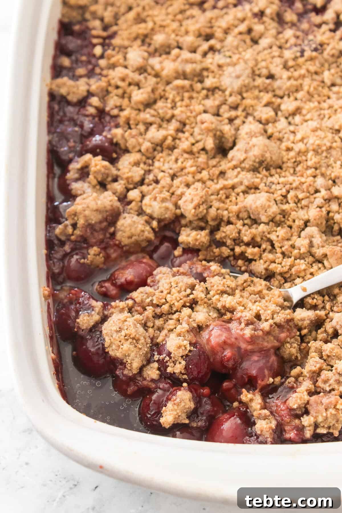 Gluten-Free Cherry Cobbler Recipe: Flaky Crust & Juicy Filling 7 spoon in corner of casserole dish with spoonful of gluten-free cherry cobbler after it's been baked in the oven
