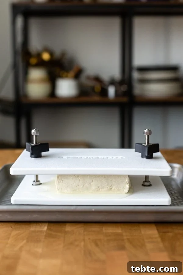How to Press Tofu: Quick Methods With and Without a Tofu Press 3 block of tofu in a white tofu press that's in a baking tray sitting on a butcher block counter