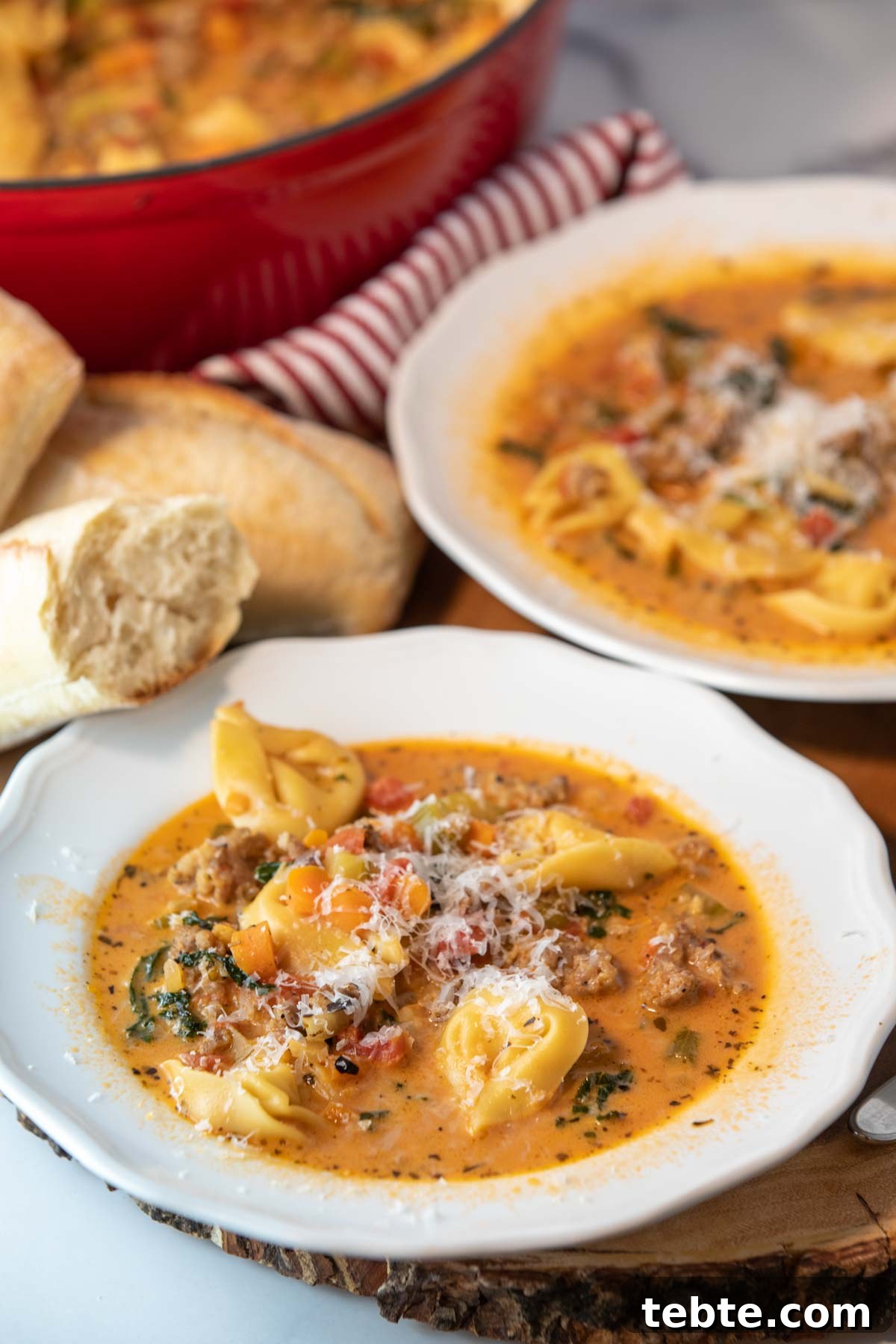 two bowls of spicy tortellini soup with bread and spoons sitting beside