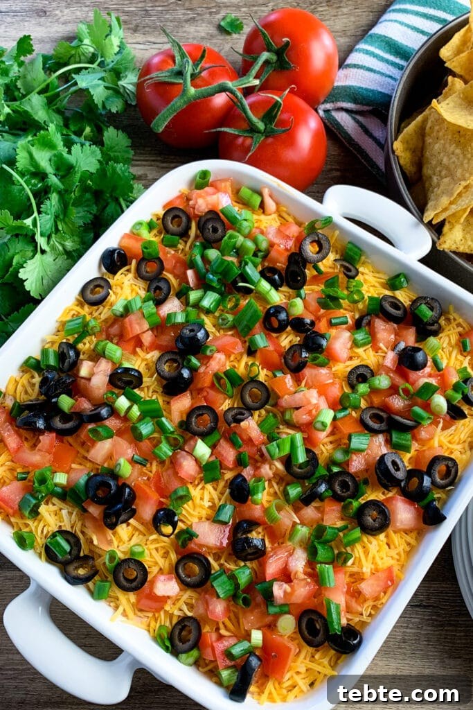 Authentic Mexican 7-Layer Bean Dip Recipe for Entertaining 2 Overhead pic of a seven-layer dip in a white baking dish garnished with olives, green onions, and tomatoes.