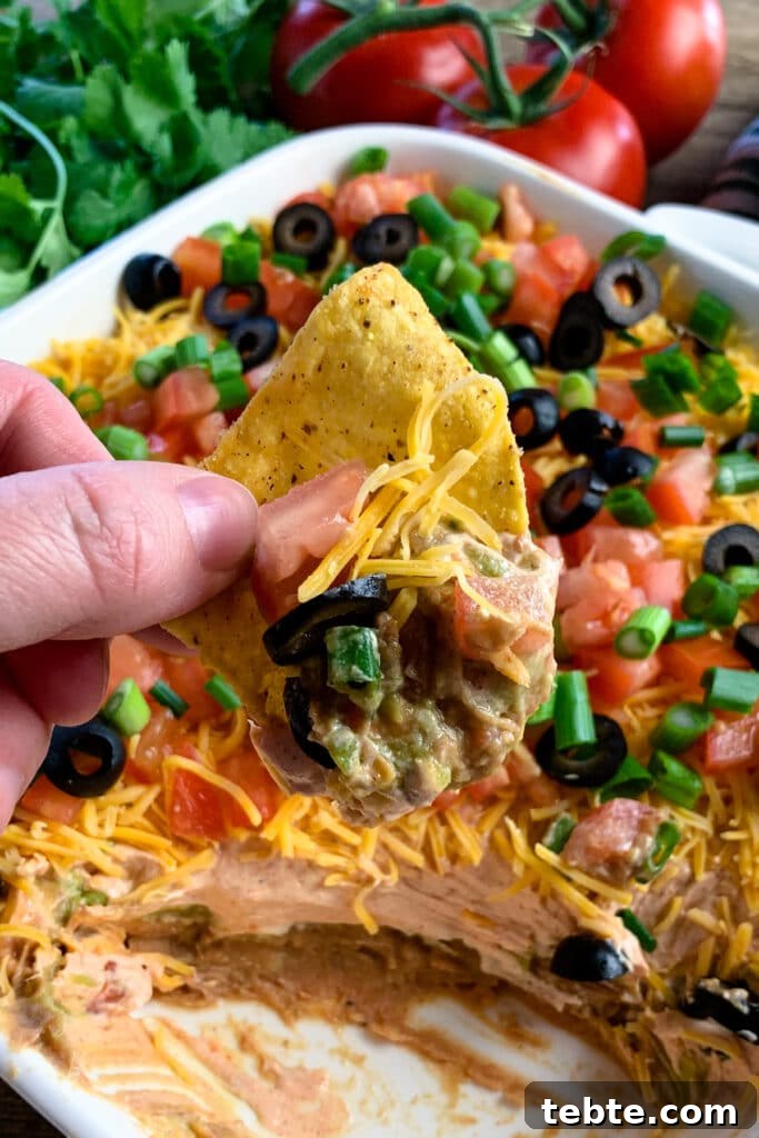Authentic Mexican 7-Layer Bean Dip Recipe for Entertaining 4 7 layer dip on a tortilla chip to show the refried beans and guacamole.