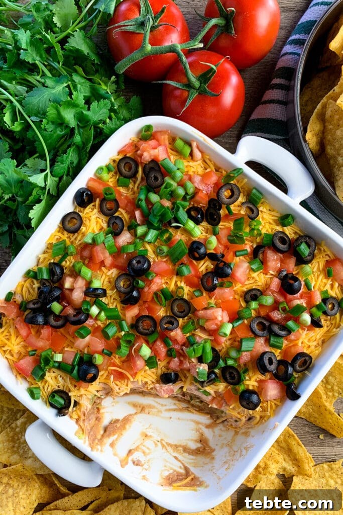 Authentic Mexican 7-Layer Bean Dip Recipe for Entertaining 5 Overhead look at 7 layer dip with a scoop taken out and tortilla chips around it.