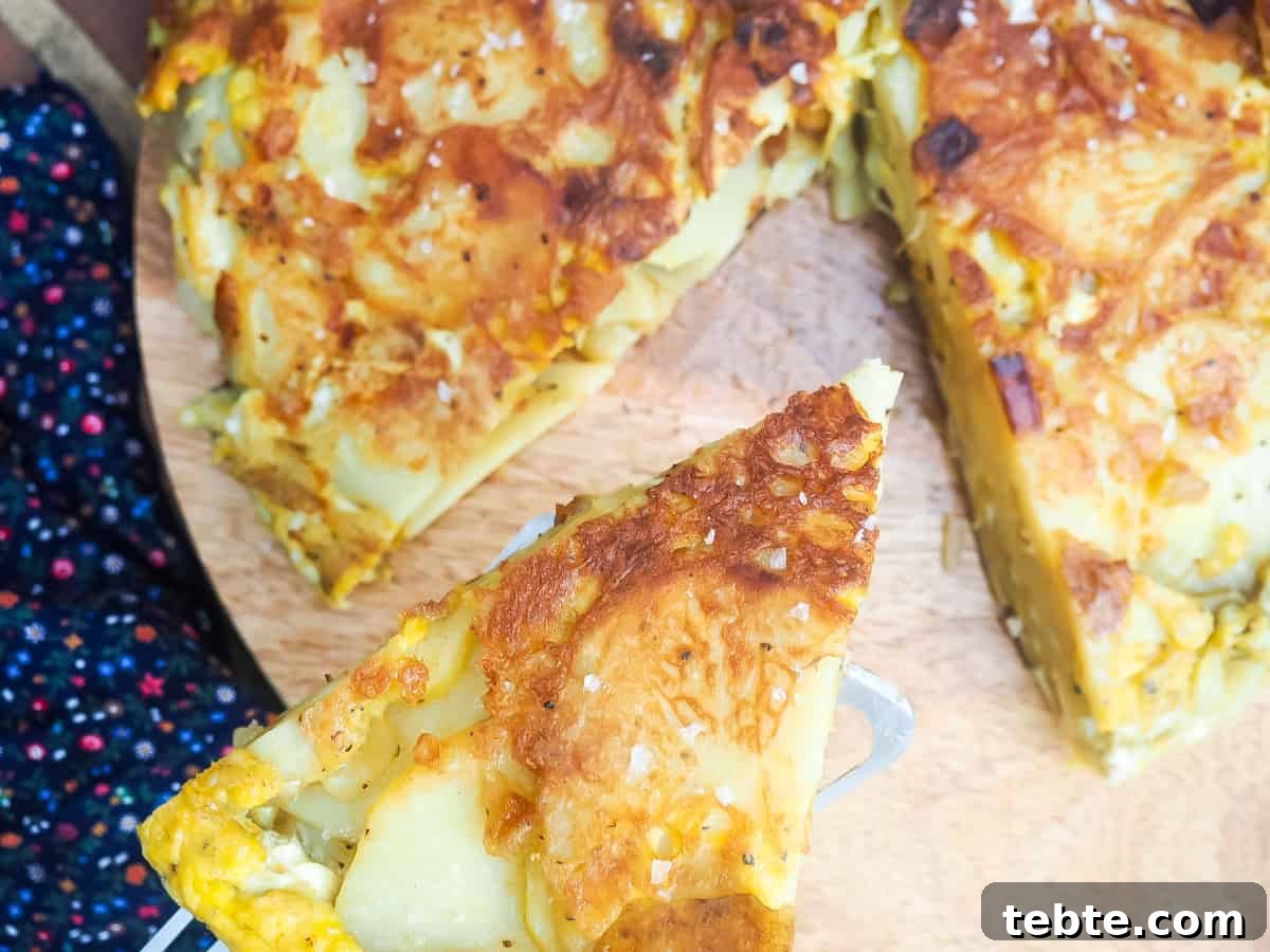 Authentic Spanish Tortilla: Traditional Egg and Potato Recipe 2 A metal spatula holding a slice of Spanish tortilla above the rest of the tortilla on a wooden cutting board.