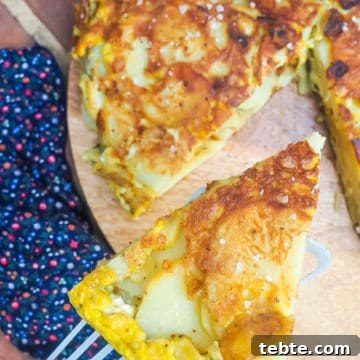 Authentic Spanish Tortilla: Traditional Egg and Potato Recipe 11 A metal spatula holding a slice of Spanish tortilla above the rest of the tortilla on a wooden cutting board.