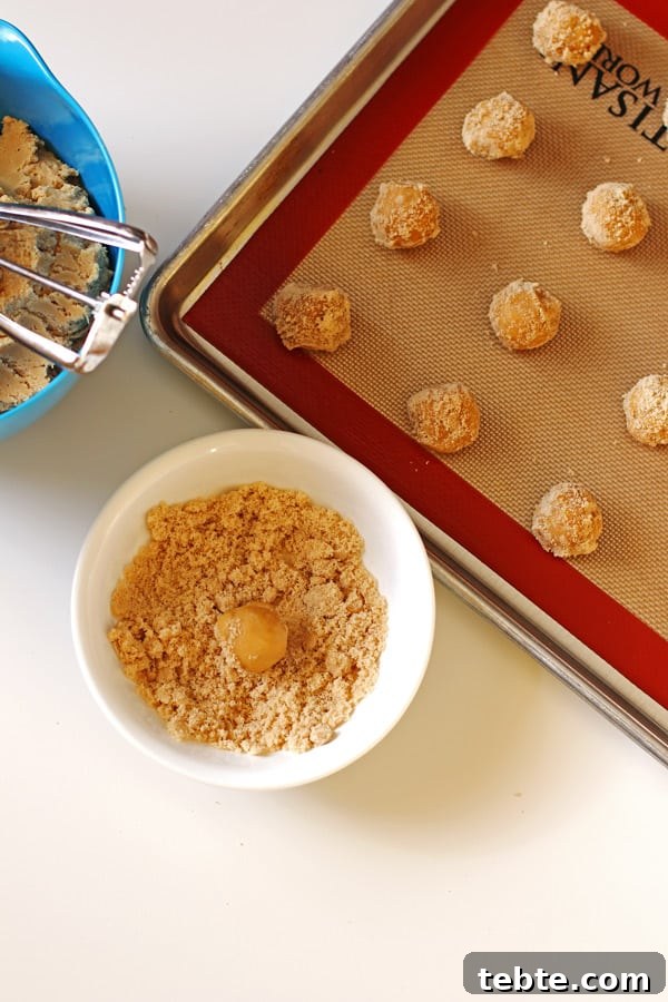 Peanut Butter Kiss Cookies Recipe — Chewy Chocolate-Stamped Treats 5 Dough balls coated in brown sugar placed on baking pan