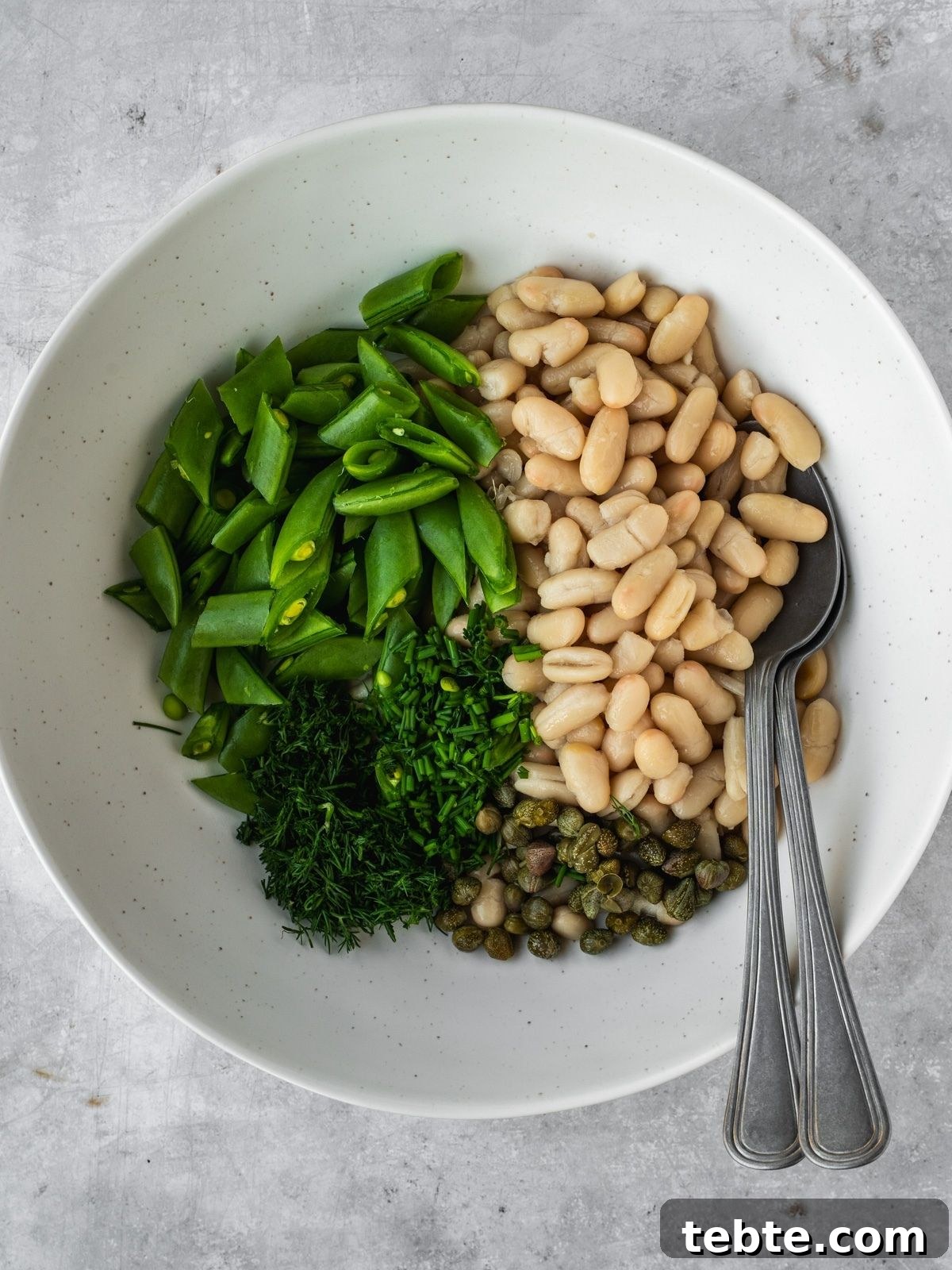 Grilled Asparagus and White Bean Salad with Lemon Vinaigrette 7 A bowl with canned white beans, chopped snap peas, capers and fresh herbs.
