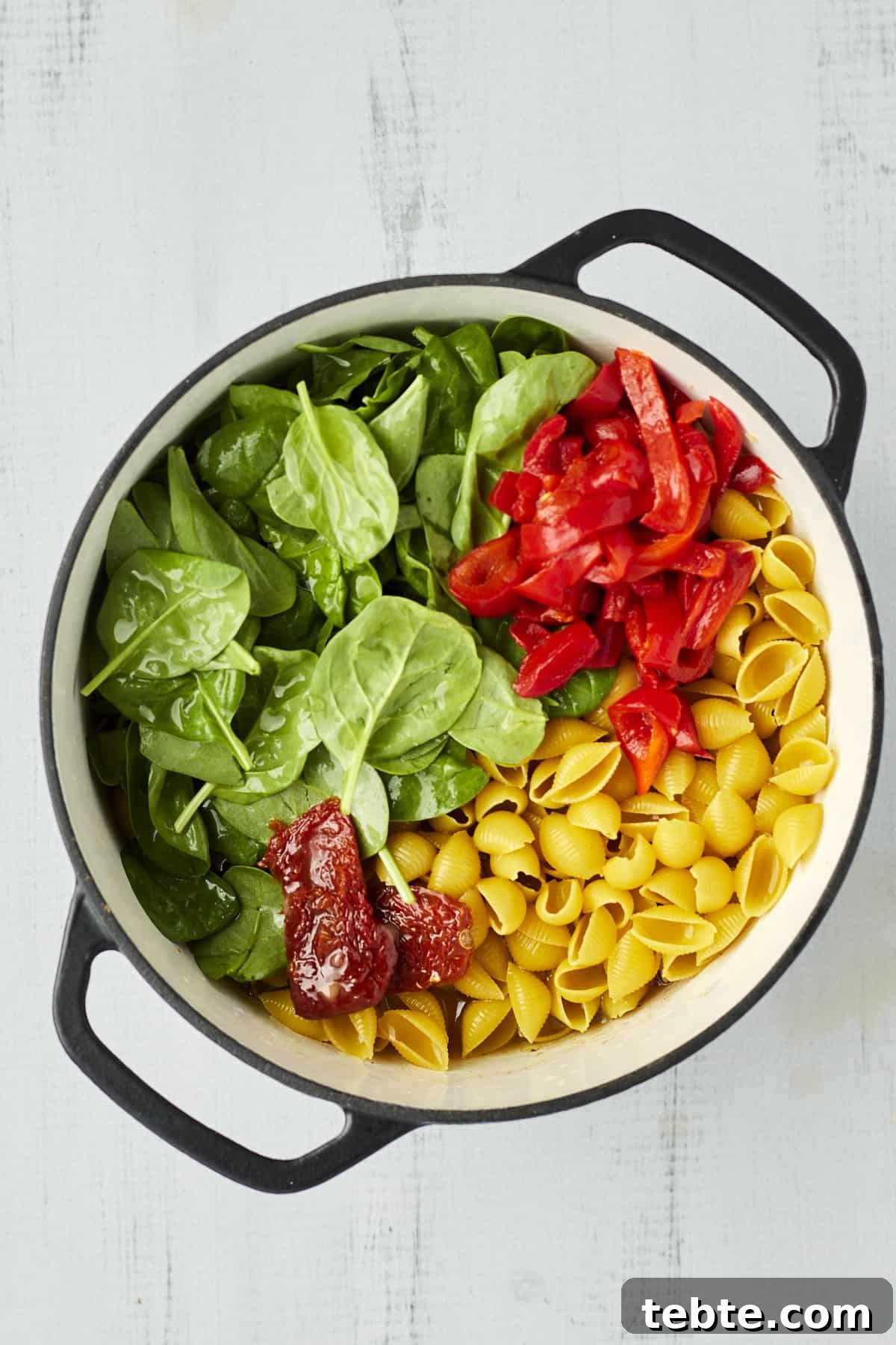Creamy Tuscan Chicken Pasta Made in One Pot 4 Cooked pasta shells, red bell peppers, spinach, and roasted tomatoes in a large pot.
