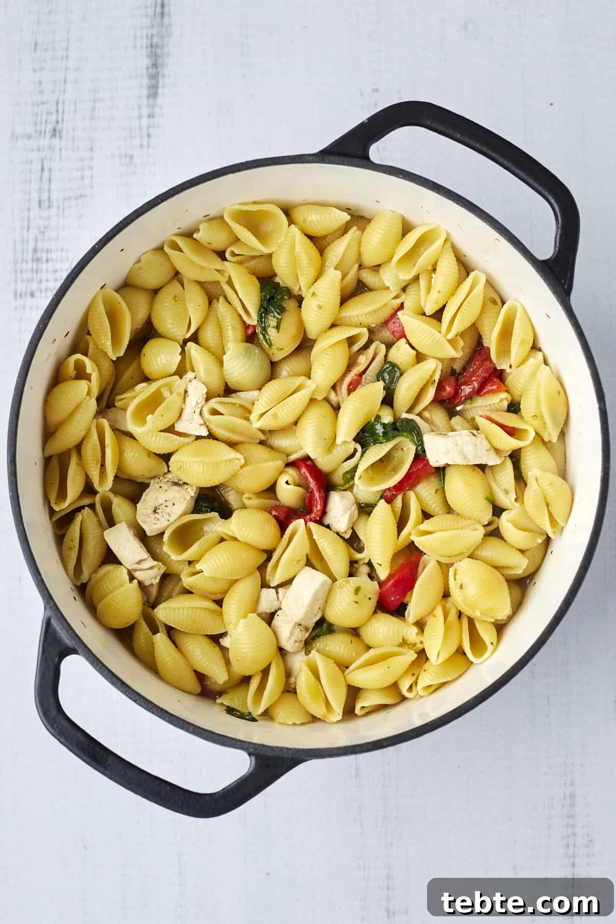 Creamy Tuscan Chicken Pasta Made in One Pot 5 Cooked pasta shells, spinach, red bell peppers, roasted peppers, and chicken in a pot.