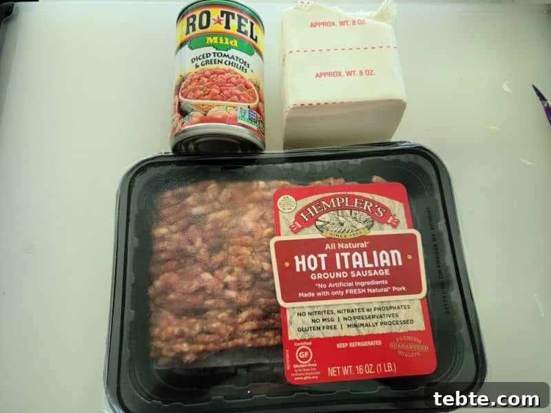 3-Ingredient Rotel and Sausage Dip Recipe 3 Can of Rotel diced tomatoes and green chilies, cream cheese, and hot Italian ground sausage on cutting board.