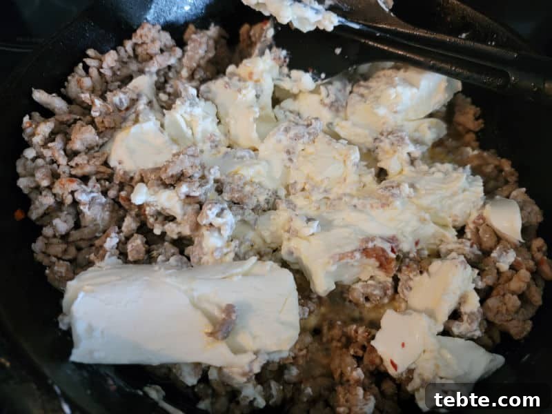 3-Ingredient Rotel and Sausage Dip Recipe 5 Cream cheese mixing into ground sausage in a cast iron skillet