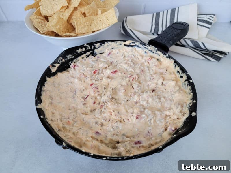 3-Ingredient Rotel and Sausage Dip Recipe 6 Velveeta dip in a cast iron skillet next to a white bowl of tortilla chips and a cloth napkin